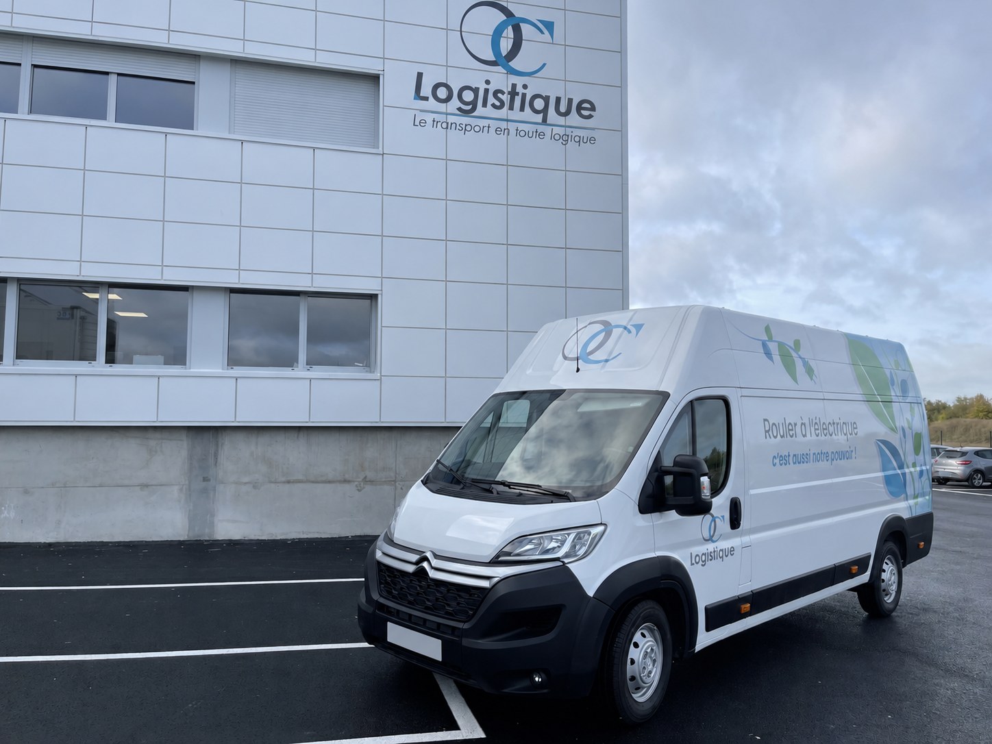 Véhicule électrique OC Logistique devant le bâtiment de l’entreprise, immatriculations masquées